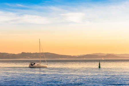 Sailboat sailing near maritime signaling buoy in Pontevedra bay at the eveningの写真素材