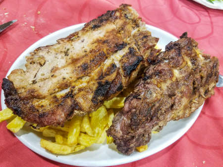 Grilled pork rib with french fries served an porcelain plateの写真素材