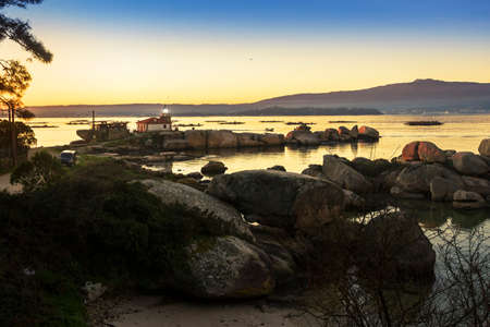 Punta Cabalo rocky coast in Arousa Island with a lighthouse lighting at dusk