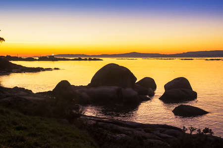 Lighthouse flash at golden dusk on the rocky coast of Arousa Islandの写真素材