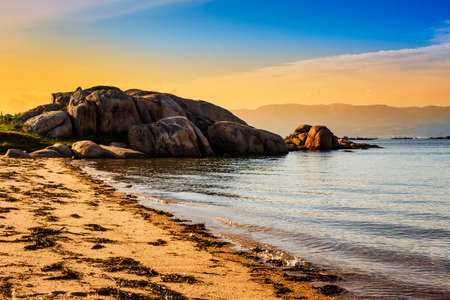 Coastal rocks on the beginning of Aguiuncho beach in Arousa Island at golden sunset