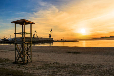 Wooden watchtower on Compostela beach in Vilagarcia de Arousa at orange sunset with harbor cranes at backgroundの写真素材