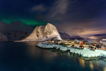 Beautiful Northern Lights in Hamnoy, Lofoten Island in Norway. Aurora Boreal over the small fishing village with its traditional red huts. Majestic green night sky.の写真素材
