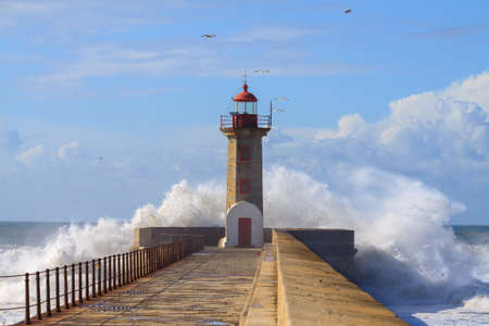 Seascape with big wave crashes at the lighthouse. Maritime landscape. Porto landmark, Portugal. Storm on the stone jetty with very rough sea.の写真素材
