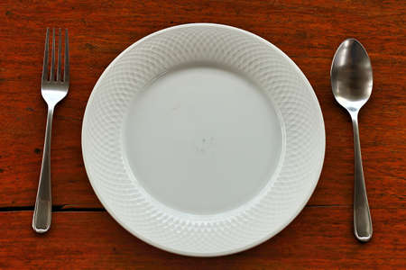 white plate, knife and fork at napkin on wooden background