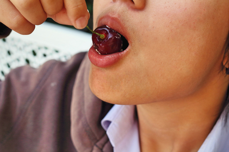 Portrait of mouth eating red cherryの写真素材
