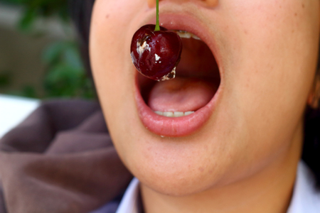 Portrait of mouth eating red cherryの写真素材