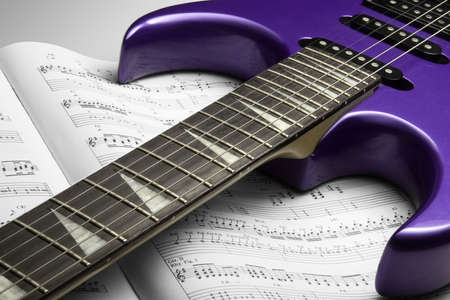 Electric Guitar on Sheet Music. A purple electric guitar on top of an open sheet music book.の写真素材