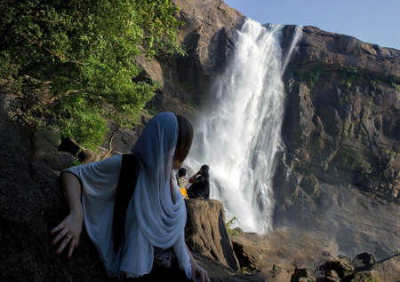 A girl in black and white dress and a waterfall named Athirapally in the background located in Kerala, Indiaの写真素材