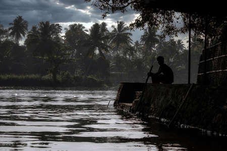A scenic view of a man sitting by the backwaters situated in Allepey town located in Kerala state,...