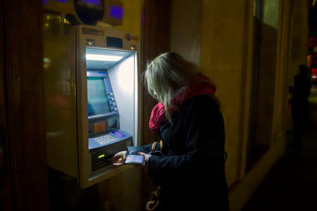 Krakow, Poland - October 25, 2014: A woman using ATM at night in winter