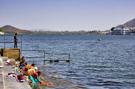 Udaipur, India - May 22, 2013: Udaipur, India - May 22, 2013: A group of Rajasthani women in Indian traditional dress washing clothes in lake Pichola behind Bagore Ki Haveliaveliのeditorial素材