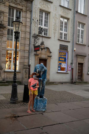 Gdansk, North Poland - August 13, 2020: A male street performer fixing mask of a girl while taking picture at city center main squareのeditorial素材