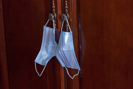 A pair of white mask showing new normal hanging next to door entrance during corona virus timeの写真素材