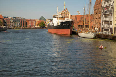 Gdansk, North Poland - August 13, 2020: A ship docked at shipyard, people enjoying kayak in motlawa...