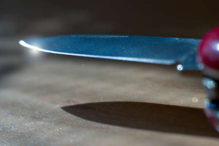 Extreme focus of pointy sharp knife with light flare at the edge. Shiny metal object against wooden background.の写真素材