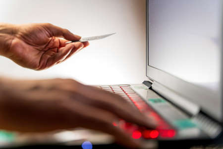 A male man hand with a credit card or debit card on left hand and making a payment by typing on...