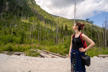 Summer hike in mountain. A young girl is looking away towards the hill landscape along the trail with a backpack. Fitness and healthy lifestyleの写真素材