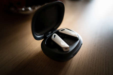 Pair of wireless earphones or earbud in its charging case isolated on wooden background. Selective focus of music hearing plugs.の写真素材