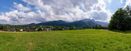 Panoramic view of green grass meadow countryside field with A shaped houses against sleeping knight tatra mountain aka as giewont and dramatic clouds located in Zakopane, South Poland, Europeの写真素材