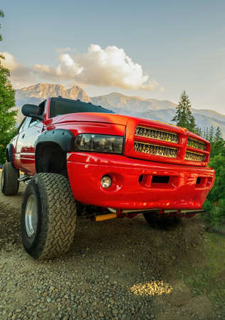 A big red monster truck with dirt tires standing on an off road against mountains and dramatic...