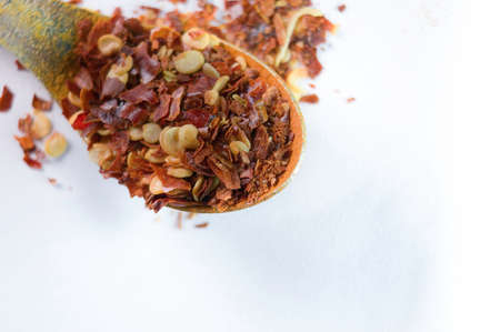 Dried chili flakes on wooden spoon against white background. Close up view of crushed red cayenne...