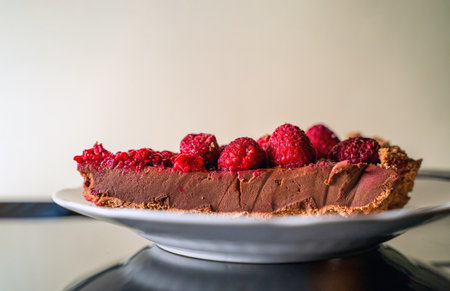 A piece of a delicious chocolate tart with raspberry on the white plate against white background,...