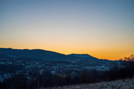 Horizontal shot of A shaped winter houses against trees and small houses on mountains during sunrise or sunset in countryside town named Limanowa in south Poland.の写真素材
