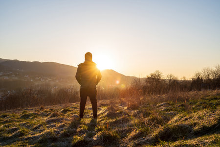 Wide angle shot of a man from behind facing a view of a landscape consists of mountain during sunrise rays in winter.の写真素材