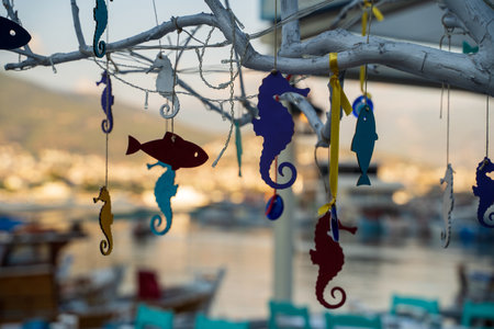 Colorful wooden decorations shaped like fish and seahorse hanging on white colored tree on sunny day in the street. Selective focus. Blurred backgroundの写真素材