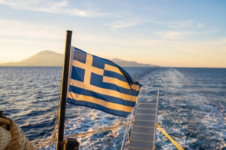 Sunset over the sea with the Greek flag in the foreground viewed from the ferry on the route to Zakynthos island in Geeceの写真素材