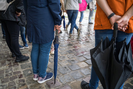 Back view of unidentified people feet wearing raincoat and carrying umbrella standing under rain against European architectureの写真素材