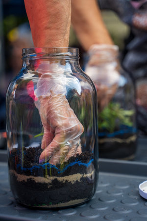 A human hand wearing gloves inside a mason jar planting a seed for environment, selective focusの写真素材