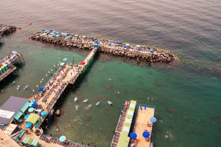 Sorrento, Italy - June 24, 2024: People relaxing on the beach on the pier and swimming in the sea on inflatable air beds in Sorrento.のeditorial素材