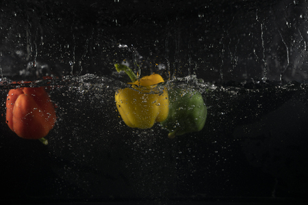 several coloured paprika falling into water splash with many bubbleの写真素材