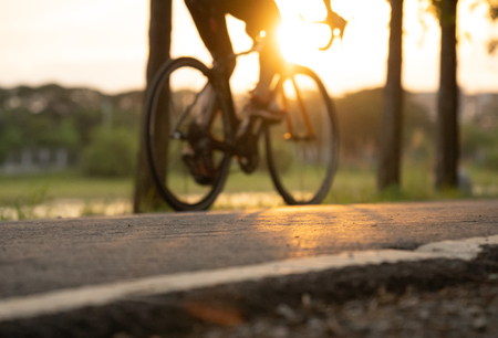 Bike at the summer sunset on road in city park. Cycle closeup wheel on blurred light at summer.の写真素材