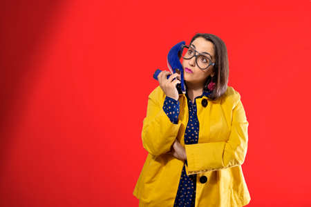 young girl on red background talking on the phone with a shoeの写真素材