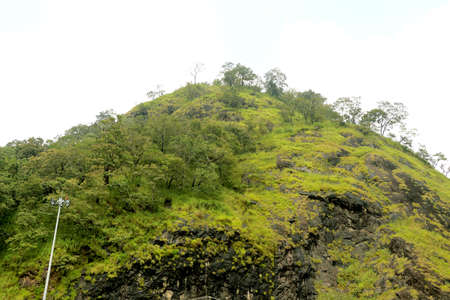 Areal view of mountain with green trees and grass on it with blue skyの写真素材