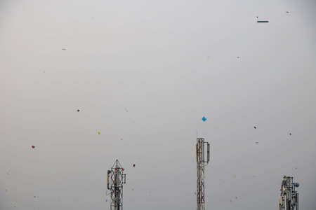 kite flying in blue sky on kite flying day in india with telephone tower at backgroundの写真素材