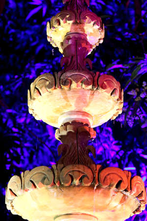 view of antique water fountain of stone with background of light on treeの写真素材