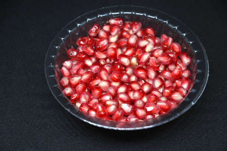 The red fresh pomegranate Seed in plastic transparent bowl on black backgroundの写真素材