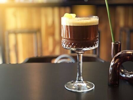 Espresso Americano coffee with ice cube and lemon orange, tonic cocktail in wine glass on table,...