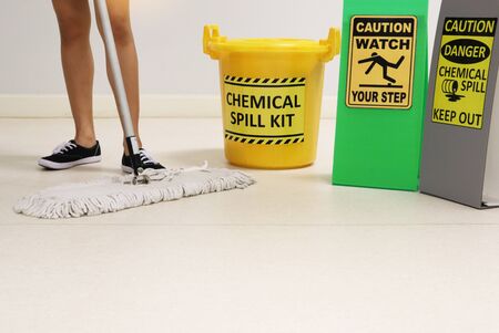 Janitor cleaning floor in medical service room or laboratory with caution tag sign watch your step and chemical spill out beside chemical spill kit yellow bucket for response chemical spill out cases.の写真素材