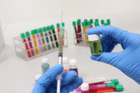 Vial glass bottle and syringe with green solvent or solution handle in hands wear nitrile blue gloves, with colorful cell culture tube, biotechnology analysis experiment for testing vaccine antivirus.の写真素材