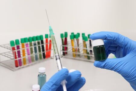 Vial glass bottle and syringe with green solvent or solution handle in hands wear nitrile blue gloves, with colorful cell culture tube, biotechnology analysis experiment for testing vaccine antivirus.の写真素材