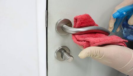 Janitor wear surgical gloves cleaning the door handles with an antiseptic alcohol sanitizer during a viral epidemic corona virus (COVID-19) pandemic. Ethanol 70% sterile cleaner protecting inflected.の写真素材
