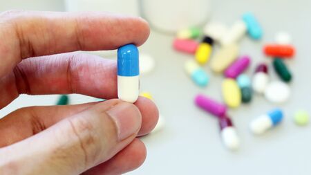 Woman hands holding blue-white capsule of Dicloxacillin, used to treat bacterial infection or treat patient who have pneumonia. Penicillin antibiotic isolated with colorful drugs, pills and tablets.の写真素材