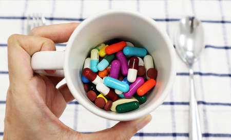 A cup of medicines hold in woman hand isolated in check white-blue pattern with fork and spoon ready to take for a patient who has to take medicines to inspire them, can use as a medical background.の写真素材