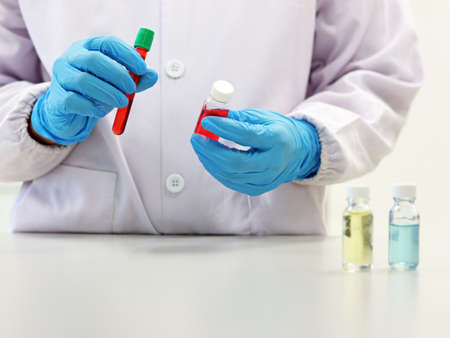 The scientist holding cell culture tube cover with green caps has red solvent or solution wear...
