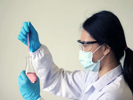 The scientist wears PPE and holds an Erlenmeyer flask laboratory, with pale pink solvent solution from dropping reaction indicator acid titration experiment, analysis compounding in wastewater sample.の写真素材